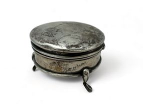 A silver circular hinged trinket box, fabric lined and on three legs. Condition: dents to lid,