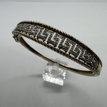 A 9ct yellow and white gold hinged "Greek Key" design bangle set with 43 eight cut diamonds.