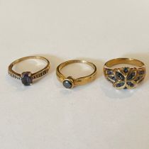 A collection of three 9ct yellow gold gem set rings Featuring a sapphire set flower shape dress