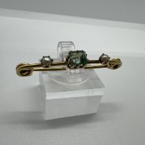 A seed pearl and emerald bar brooch, featuring an emerald cut stone, flanked by two seed pearls.