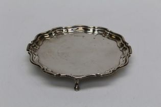 J and T, an early 20th century silver waiter, having a pie crust rim, raised on three scroll feet.