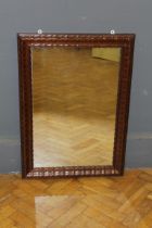 An Edwardian mahogany veneer wall mirror, the wavy stepped cushion frame enclosing a rectangular