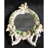 A late 19th century Dresden porcelain oval mirror encrusted with roses and applied with putti,