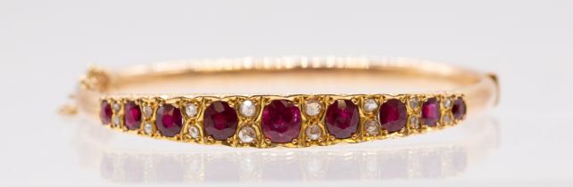 An Edwardian ruby set gold hinged bangle comprising a row of graduated grain set off round mixed cut
