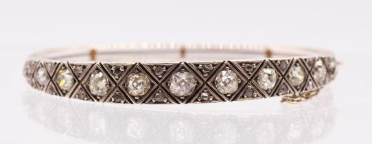 An Edwardian diamond and gold hinged bangle, comprising a platinum set with eleven graduated old