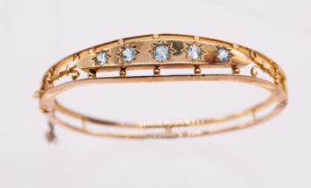 An Edwardian blue topaz and 15ct gold hinged bangle comprising a row of star set round mixed cut