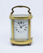 An early 20th Century gilt metal mounted oval shaped carriage clock, white enamel dial with Roman
