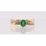 An emerald and diamond crossover set 18ct gold ring, comprising central oval mixed cut emerald