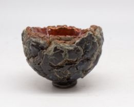 A 20th century studio pottery footed bowl, being of rock like form/design with lava red painted