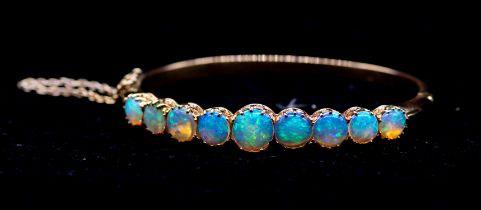 An opal and 18ct gold hinged bangle, comprising nine graduated round cabochon opals, with blue and