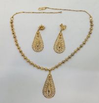 An Indian 22ct. gold pendant choker pendant necklace with drop earrings en suite, having chain of