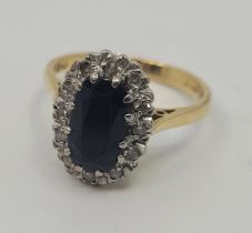 An 18ct. gold, sapphire and diamond cluster ring, set mixed oval cut sapphire to centre bordered