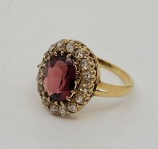 A precious yellow metal, garnet and diamond cluster ring, set oval mixed cut garnet to centre