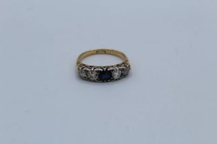 An 18ct stamped diamond and sapphire half hoop ring featuring a round mixed cut sapphire and four