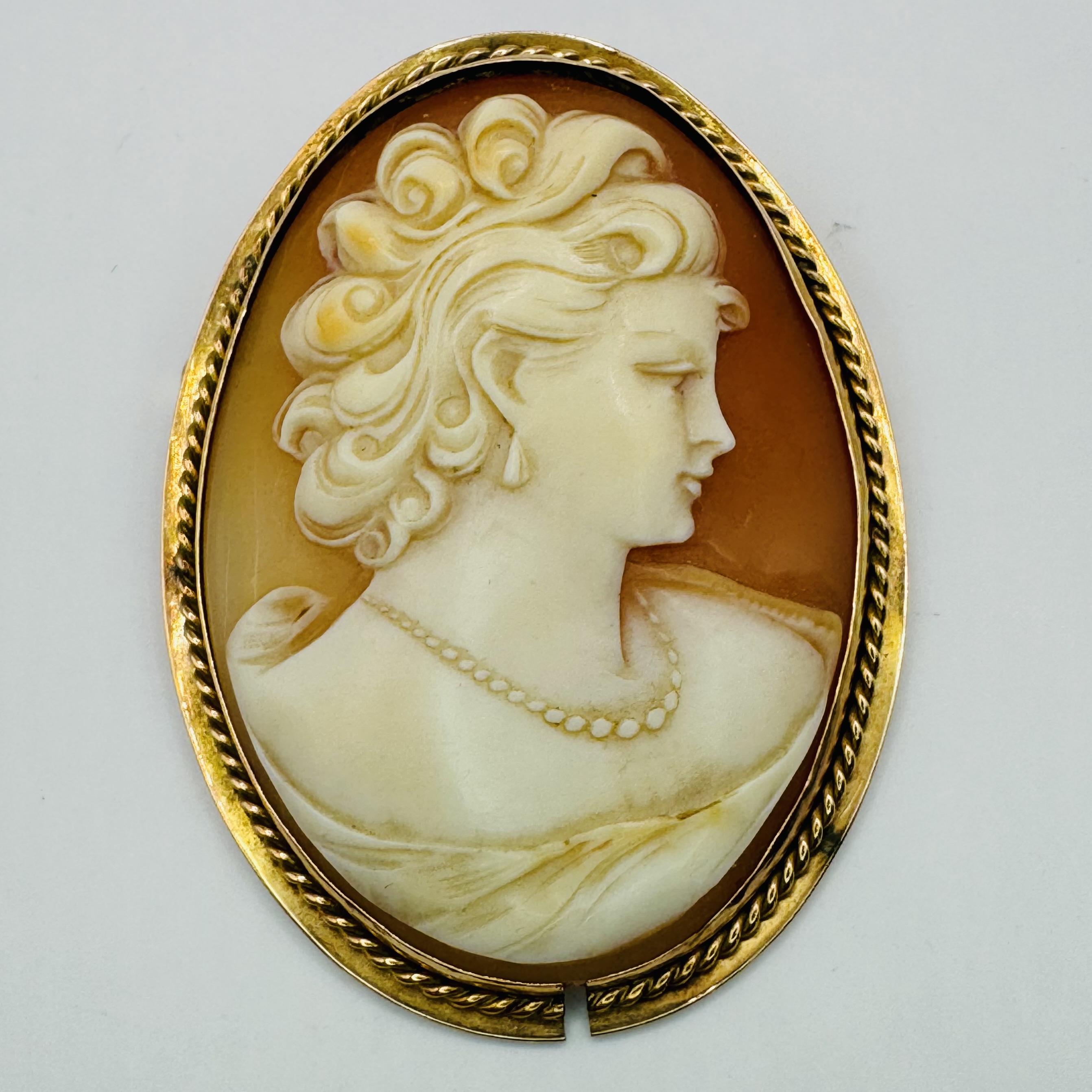A shell cameo brooch/pendant, stamped "14K" in yellow precious metal. The cameo features the