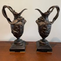 A pair of large heavy bronze Bacchanalian ewers with entwined serpent handles, standing on black