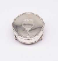 A George V silver circular ring box, shaped border on three supports, the hinged cover engraved with