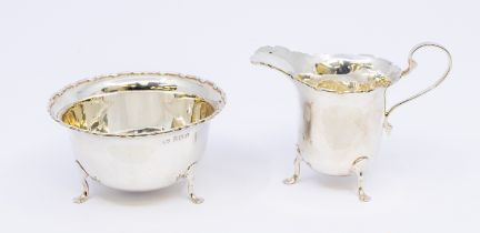 A George V silver matching sugar bowl and milk jug, both with three feet and angular designed