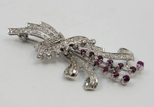 A precious white metal, diamond and ruby floral spray brooch, set eleven graduated mixed round cut