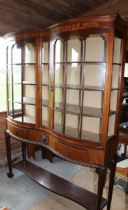 An early 20th century mahogany serpentine fronted glazed display cabinet raised on ball and claw