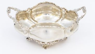 An Edwardian silver twin handled sugar bowl of oval stylised form, on four splayed elaborate foliage