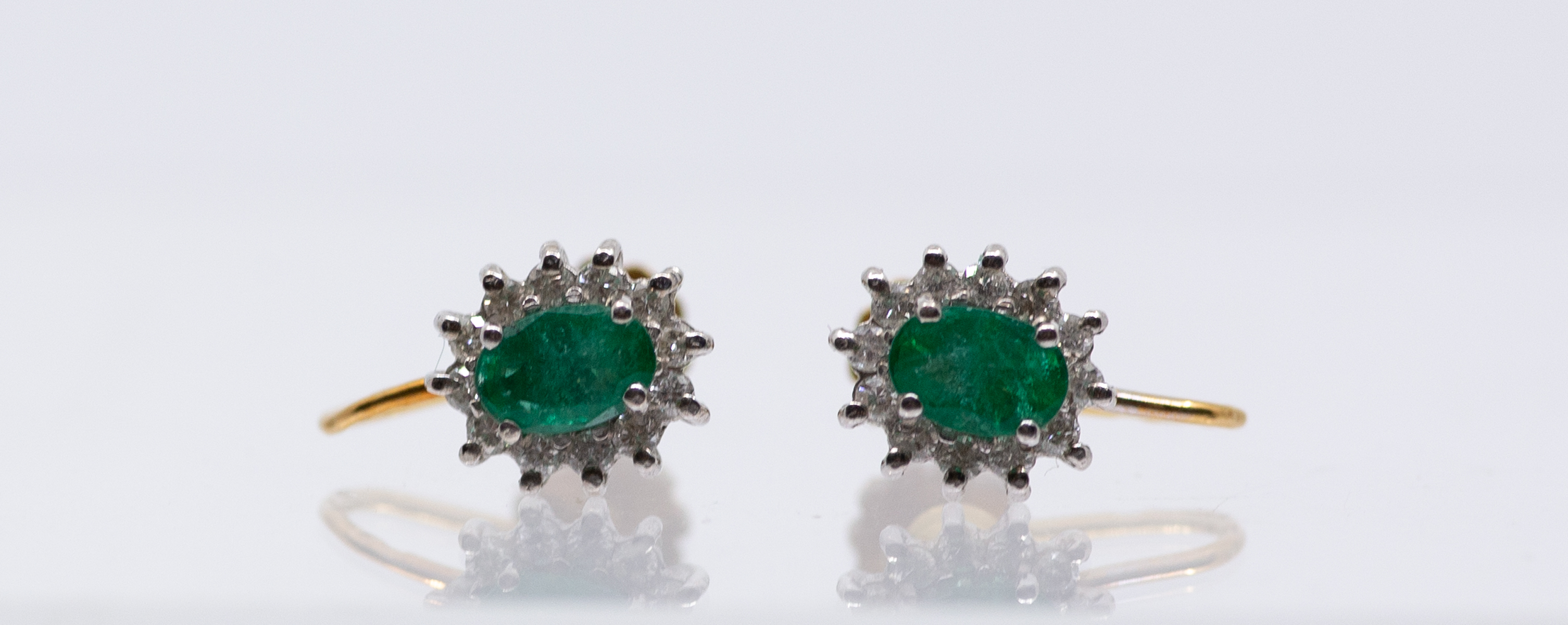 A pair of emerald and diamond 18ct gold cluster earrings, comprising an oval mixed cut emerald