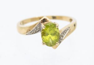 A peridot and diamond 9ct gold ring, comprising a cross over design set to the centre with an oval