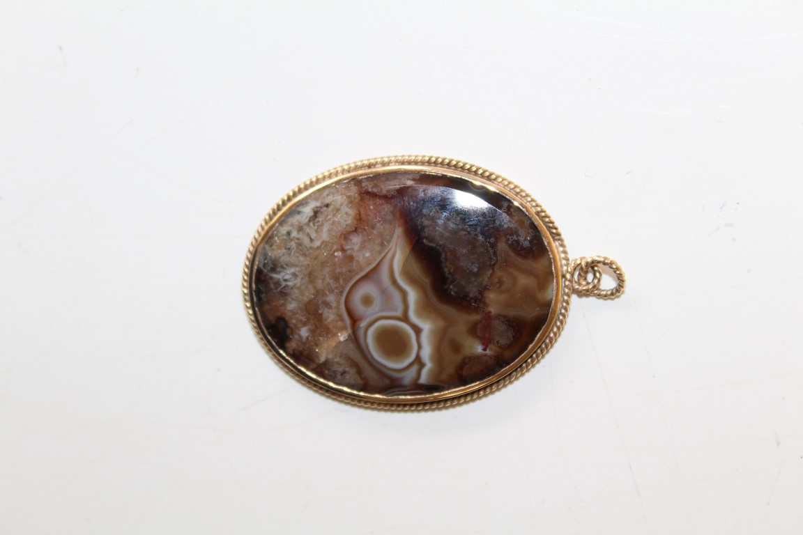 A picture agate plaque pendant in unmarked precious yellow metal bezel with twist decoration.