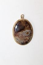 A picture agate plaque pendant in unmarked precious yellow metal bezel with twist decoration.