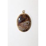 A picture agate plaque pendant in unmarked precious yellow metal bezel with twist decoration.