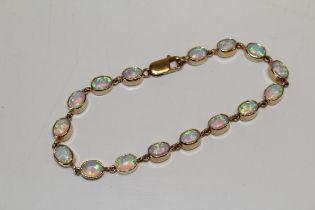 A 9ct yellow gold opal line bracelet, set with 16 cabochon opals, bezel set. Approximate length