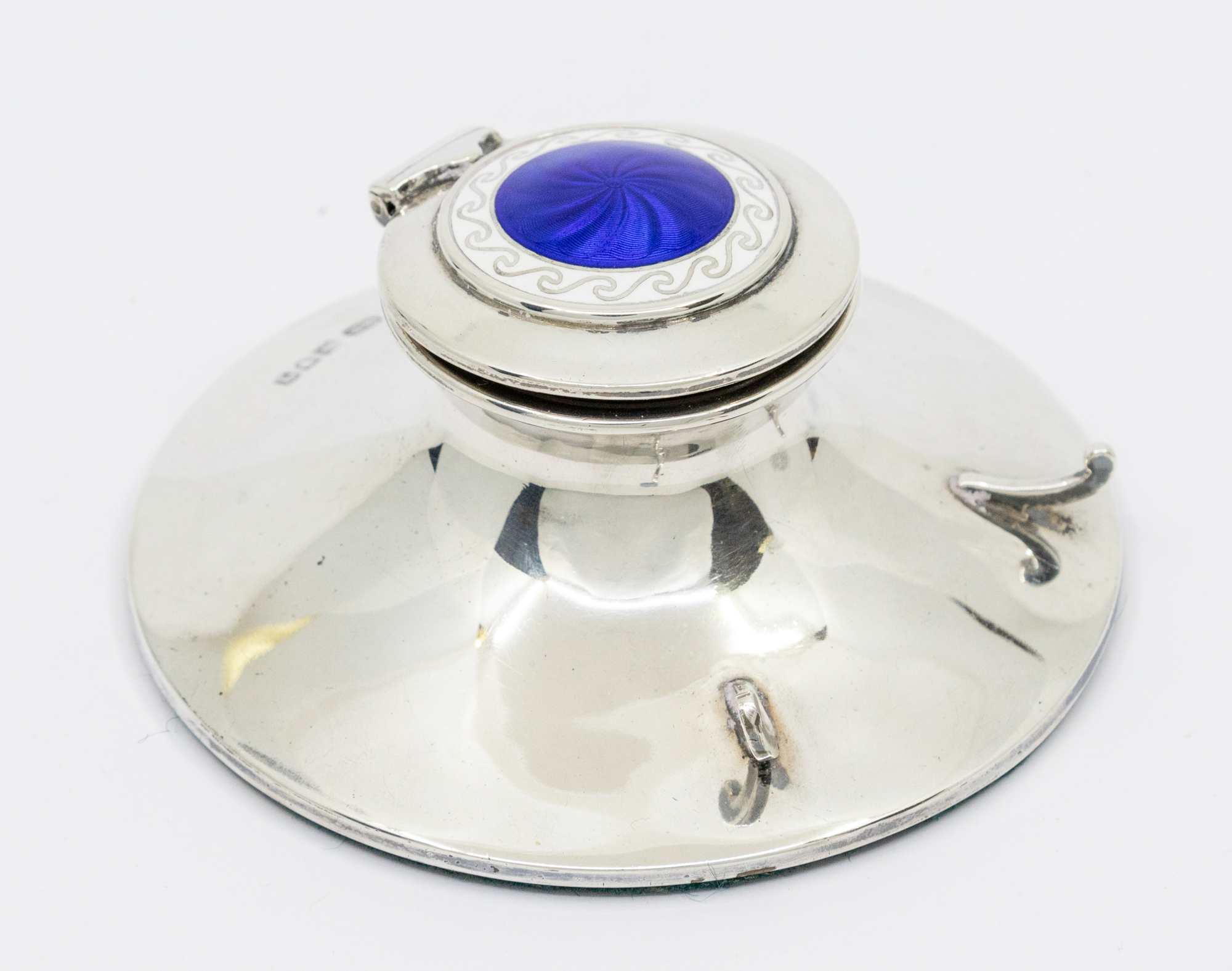 A George V silver and enamel ink well, on circular base with two curved supports for pen holder, the