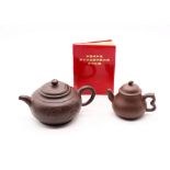 A Yixing clayware Zhi Sha tea pot along with another clayware tea pot and Chinese little red book.