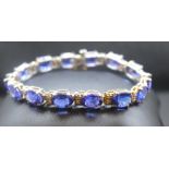 A tanzanite and diamond set 14ct white gold line bracelet, comprising a row of fourteen claw set