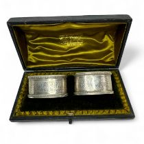 A pair of bright cut decoration silver napkin rings, with vacant cartouches, in fitted case.