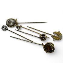 A collection of six stick pins.  Engraved crystal, gold knot, horseshoe, star engraved stone,