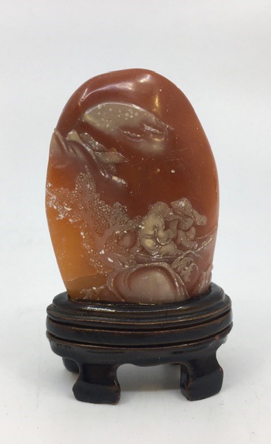 A Chinese relief carved orange hardstone, depicting two figures in a boat with prunus tree and