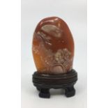 A Chinese relief carved orange hardstone, depicting two figures in a boat with prunus tree and