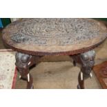 An Indian carved occasional table, the oval top with relief carved central section on elephant
