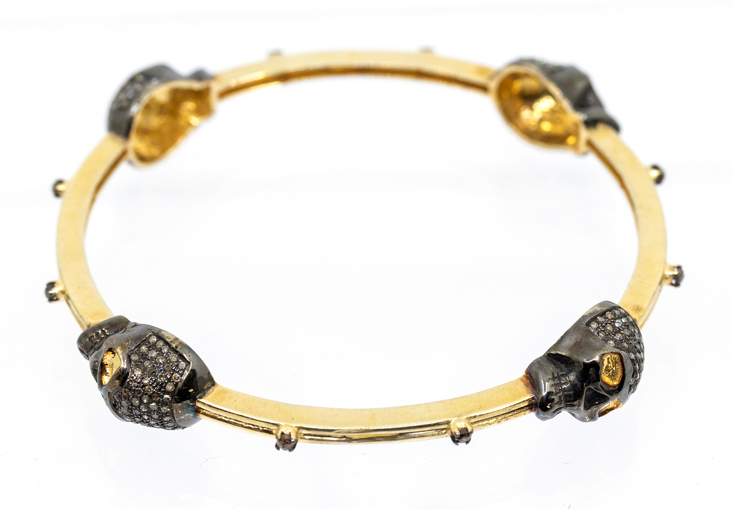 A diamond set silver gilt bangle, comprising four brown diamond set skull motifs, black rhodium