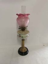 A c1900 brass columned oil lamp with painted glass well and etched cranberry glass shade. (1)