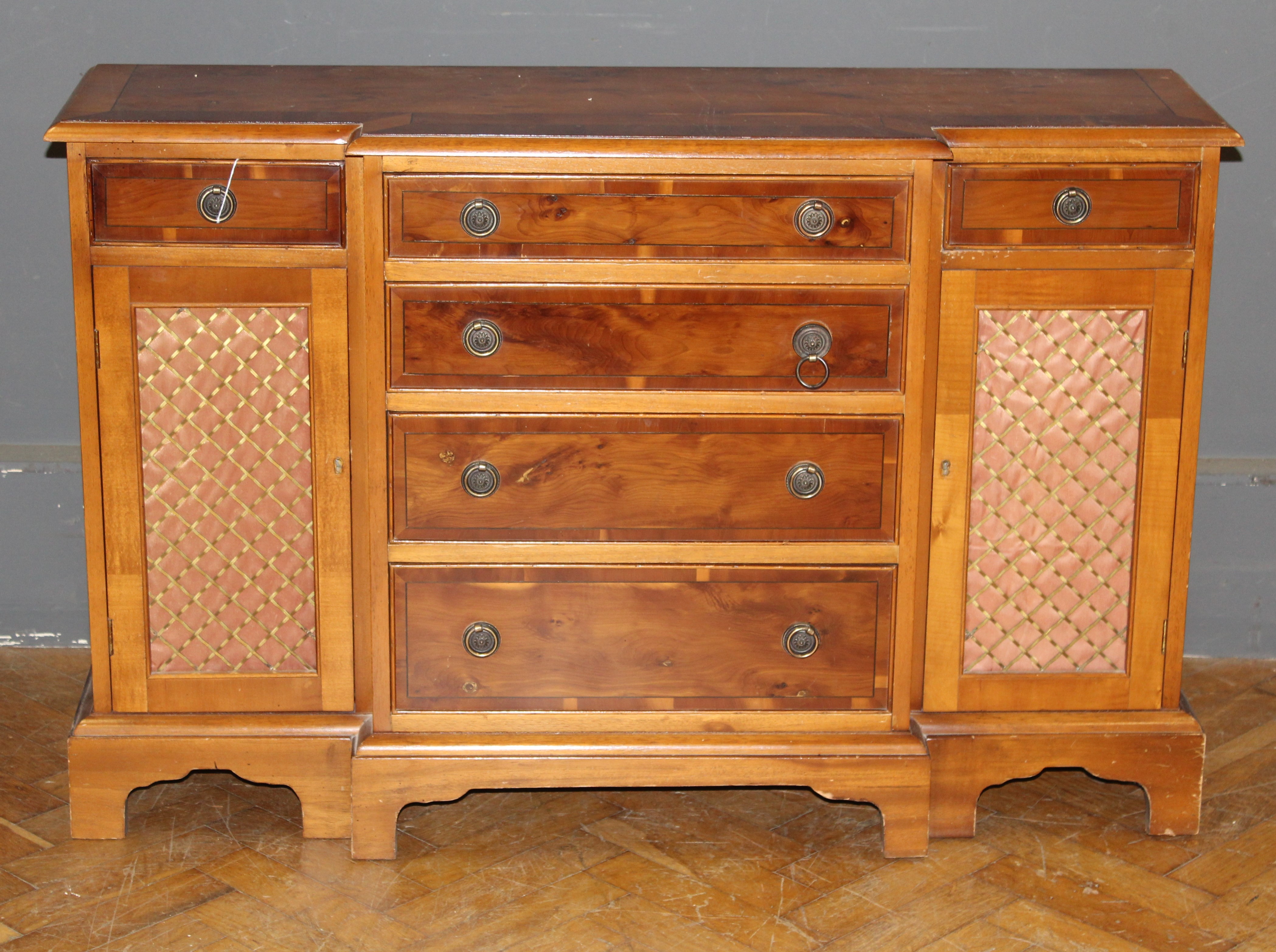 A reproduction breakfront yew veneer credenza, fitted six drawers and a pair of grilled cupboard