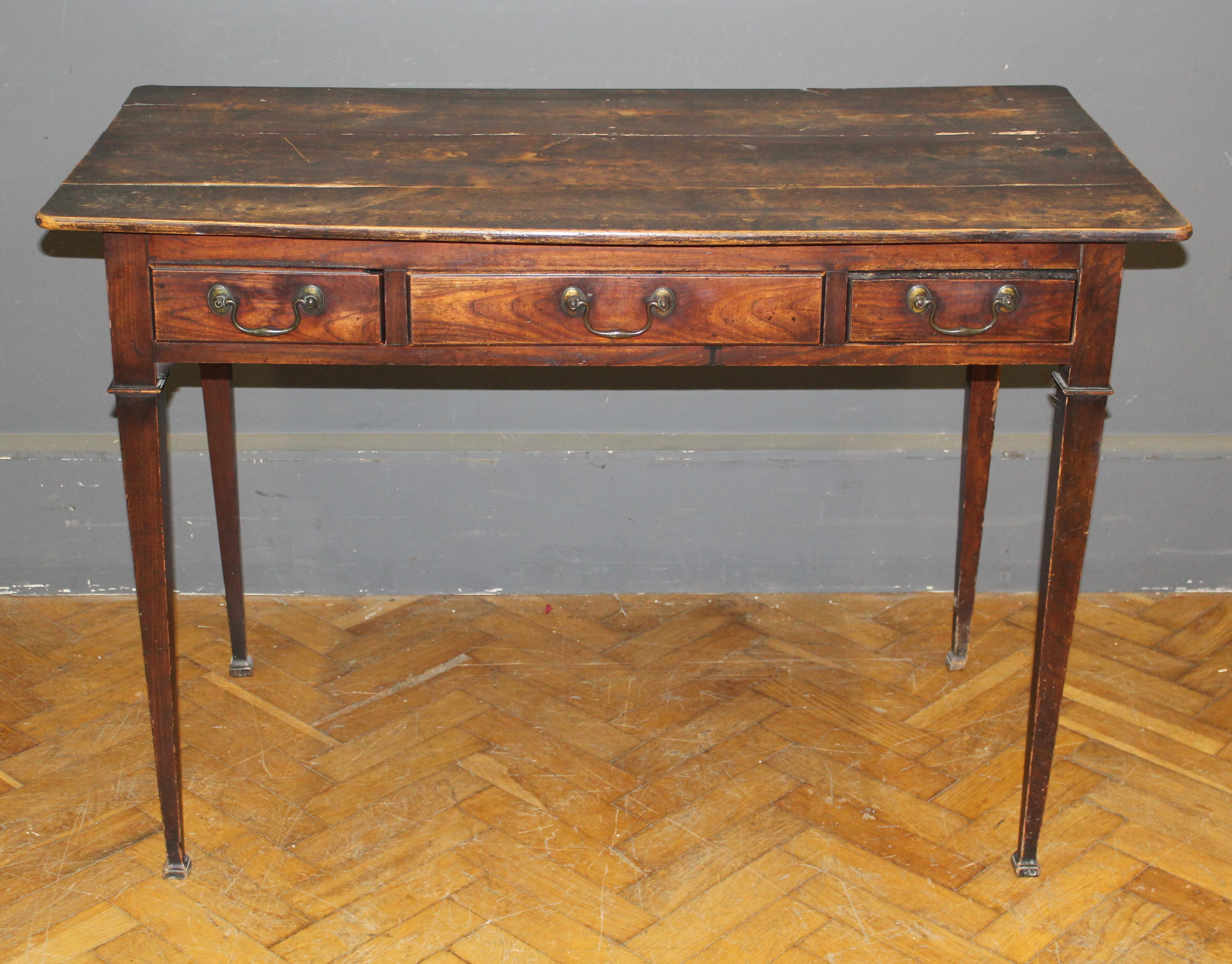 A George III elm plank top table, fitted three frieze drawers with brass swan neck drop handles,