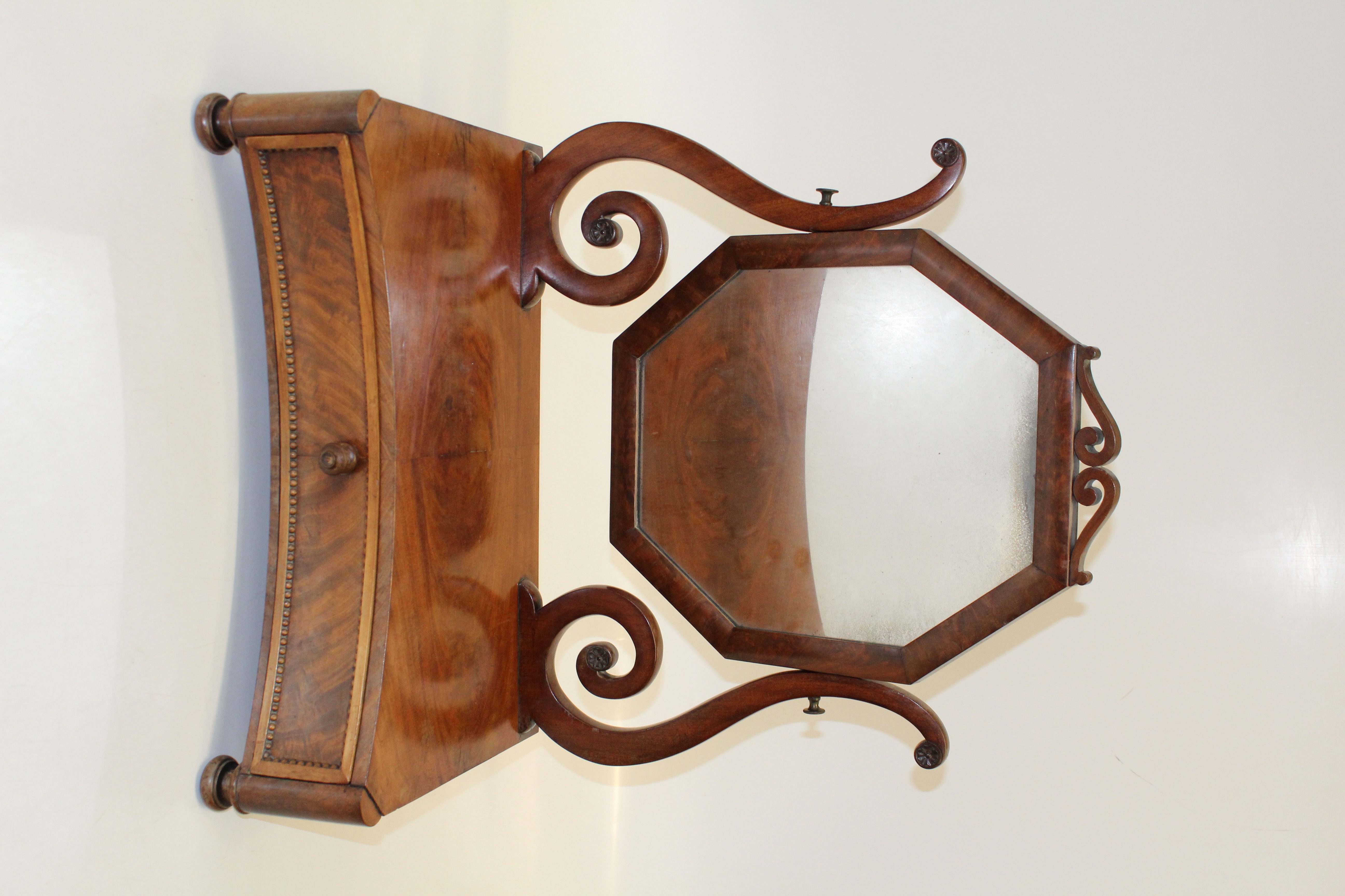 An early Victorian mahogany toilet mirror, the octagonal plate within scrolled horns, on a deep
