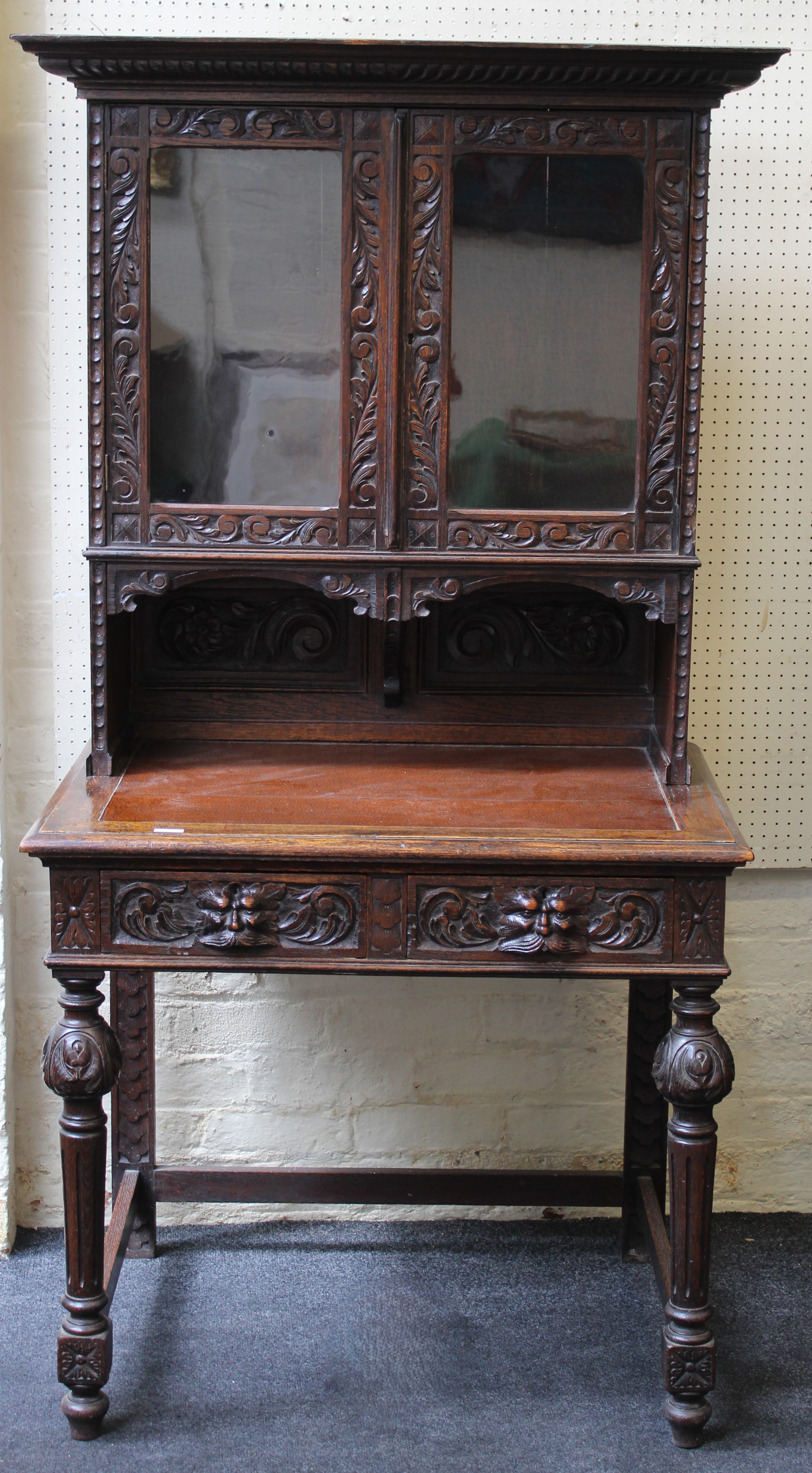 A late 19th century carved oak side cabinet, having a pair of half length glazed panel doors, over a