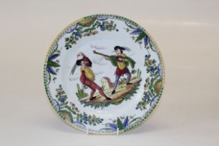 A French faience plate, hand decorated with actors within a green/blue floral border, the reverse