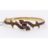 A Victorian yellow metal and Bohemian garnet hinged bangle, comprising a central rose cut garnet