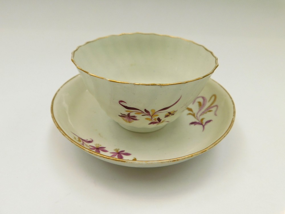 A Worcester tea bowl and saucer. Puce and gilt floral decorated, tea bowl has a twisted fluted body.