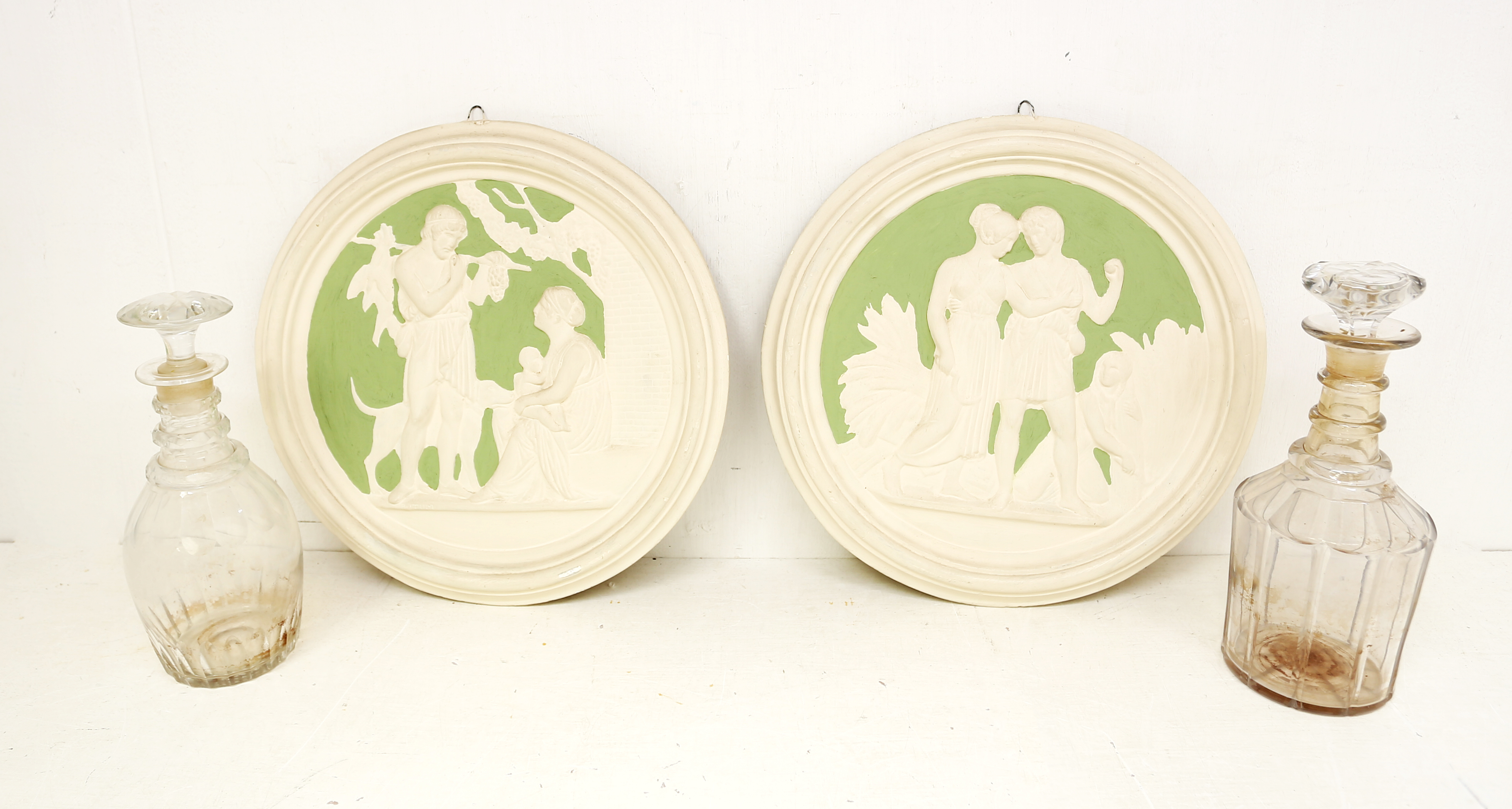 Two plaster wall plaques of classical scenes along with two George III glass decanters with