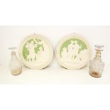 Two plaster wall plaques of classical scenes along with two George III glass decanters with